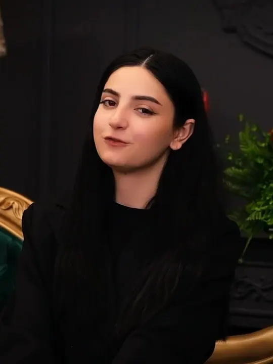 Studio portrait of a young woman beside a green velvet chair and red roses